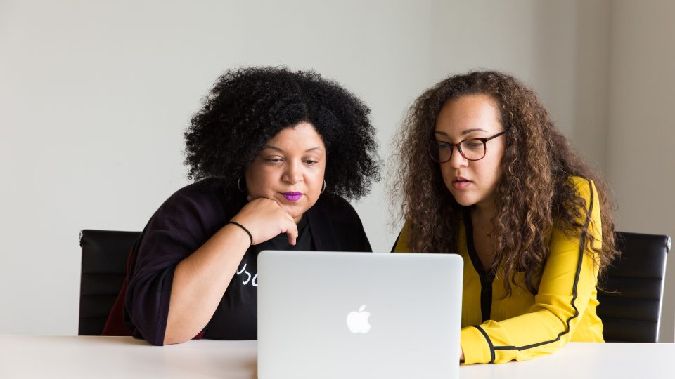 two women looking at the screen of a MacBook